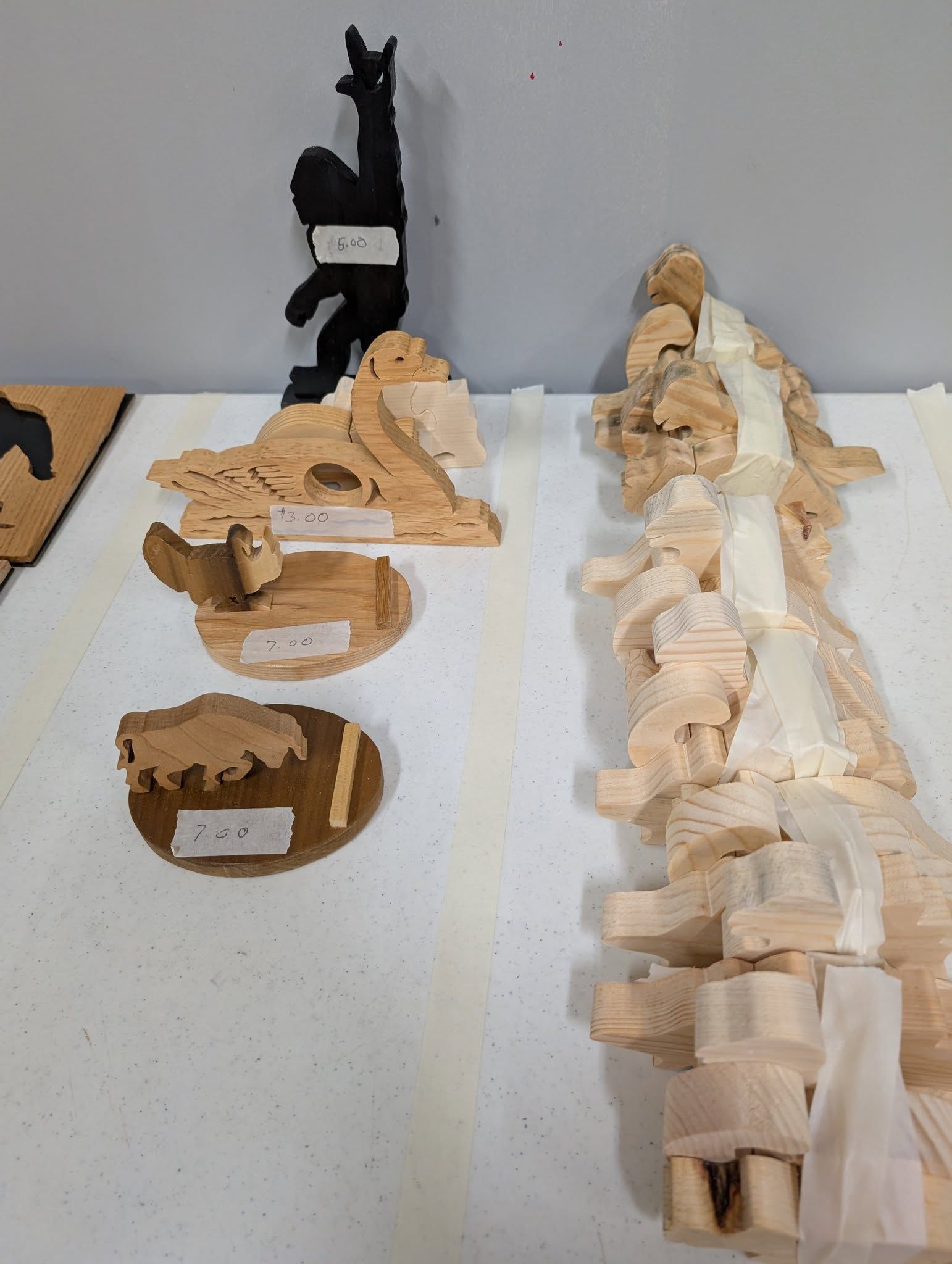 Assorted unfinished wooden animal carvings on a white surface, including a llama, owl, and waterfall.