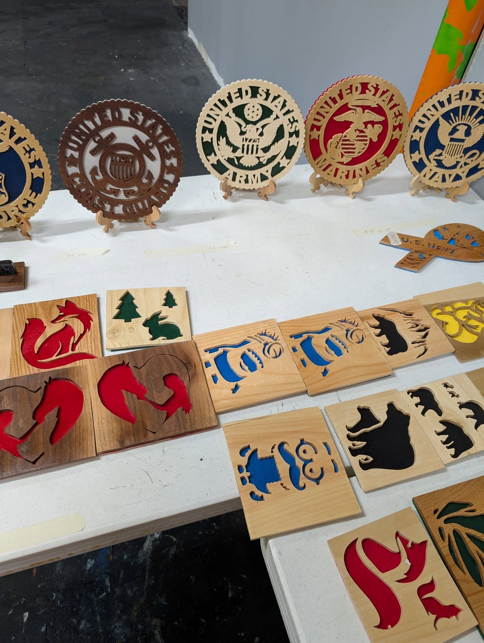 Wooden laser-cut art pieces on a table. Various designs and colors, including circles, squares, and animal shapes.