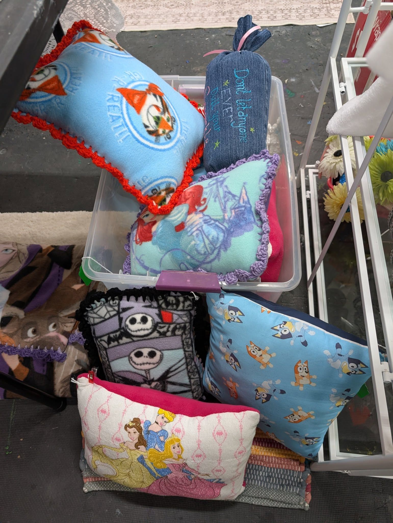 Assortment of handmade character-themed pillows in a clear bin, including Disney and Nightmare Before Christmas designs.
