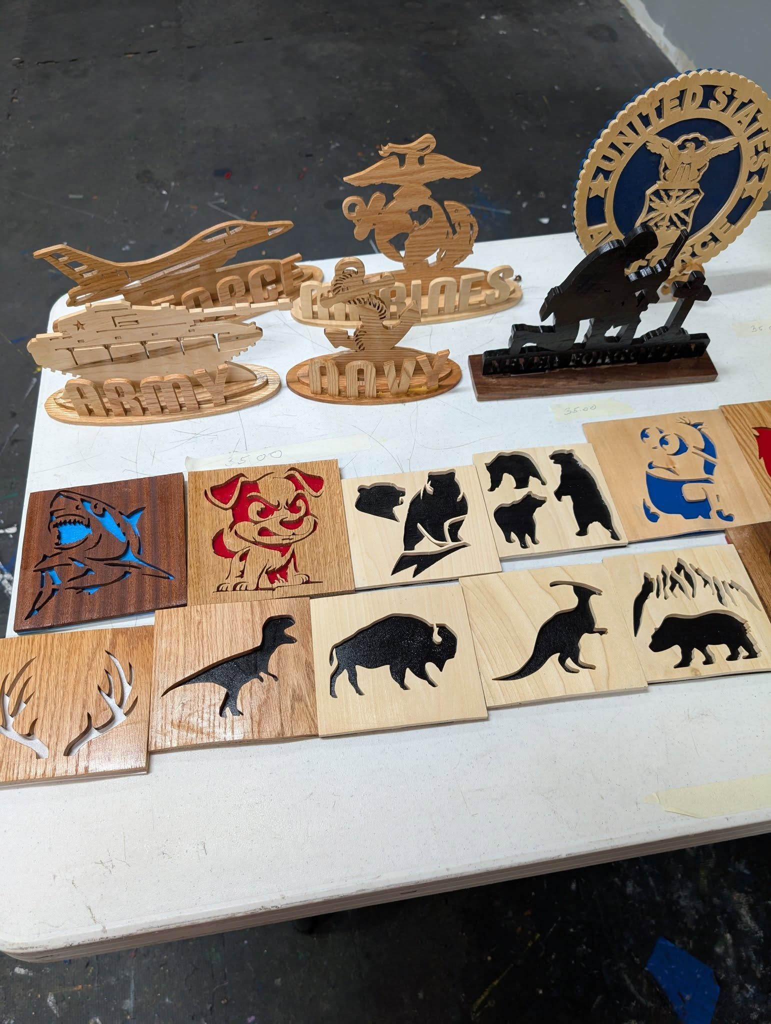 Wooden laser-cut models and plaques, including animals, a plane, and a military emblem, arranged on a white surface.