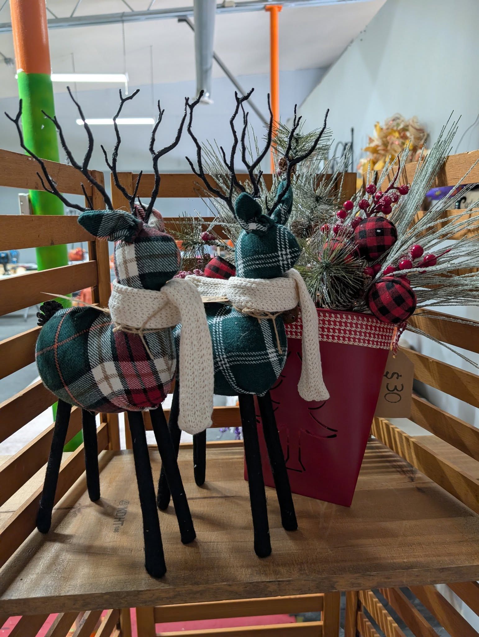 Two plaid reindeer decorations with scarves, beside a floral arrangement in a red planter.