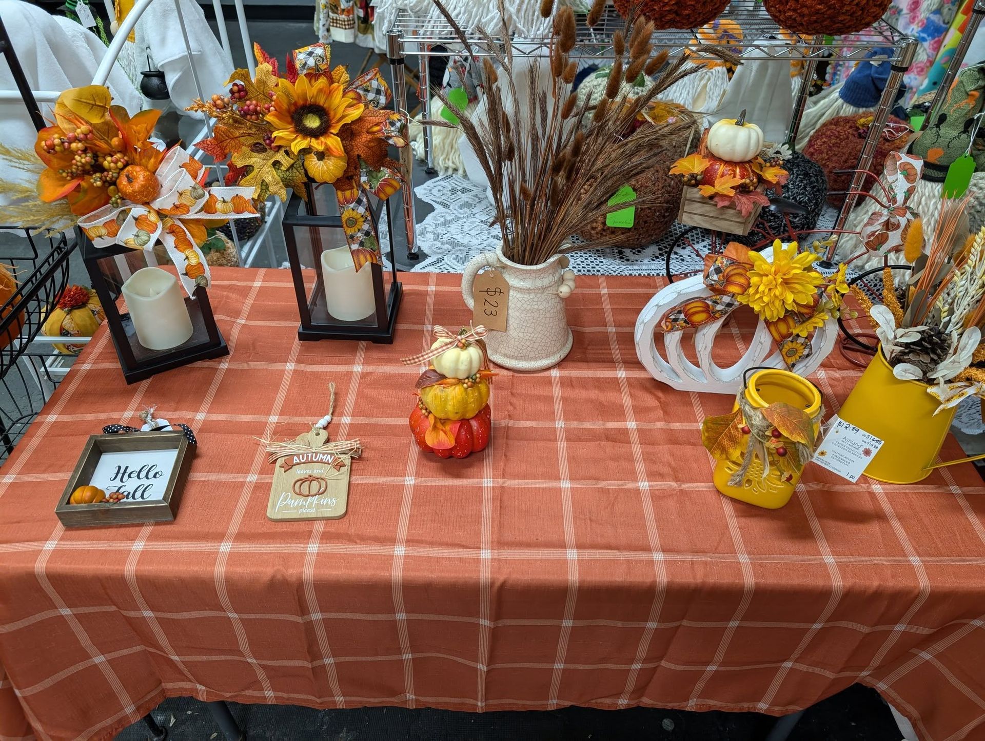 Fall decorations on a plaid orange tablecloth, including pumpkins, flowers, and candles.
