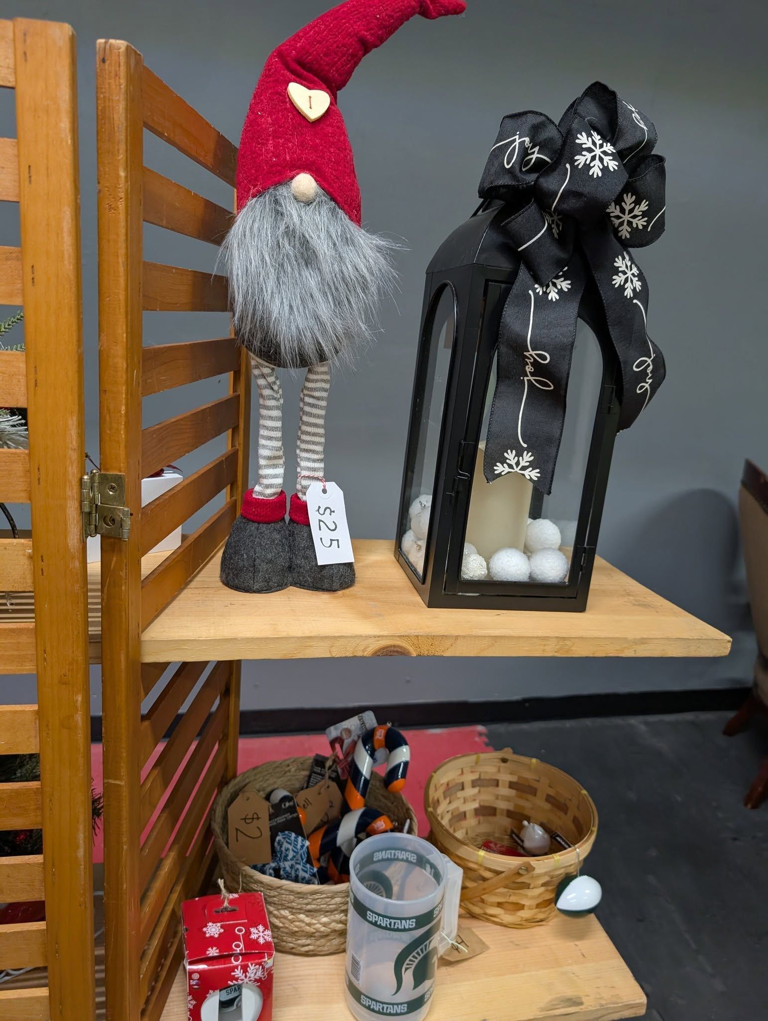 Shelf display: gnome with red hat, black lantern, baskets with items, wooden frame.