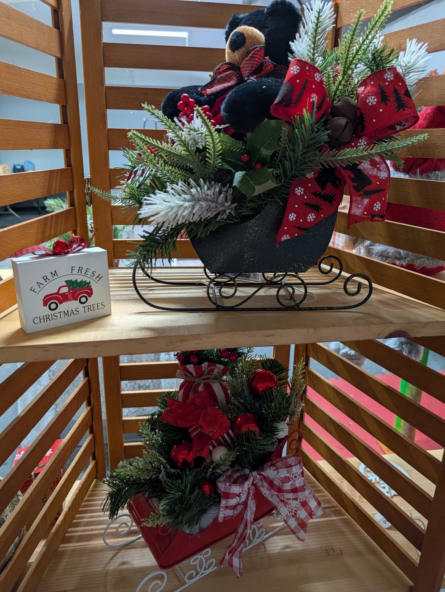 Christmas decorations displayed on wooden shelves: black bear, sleigh, gift box, and floral arrangements.
