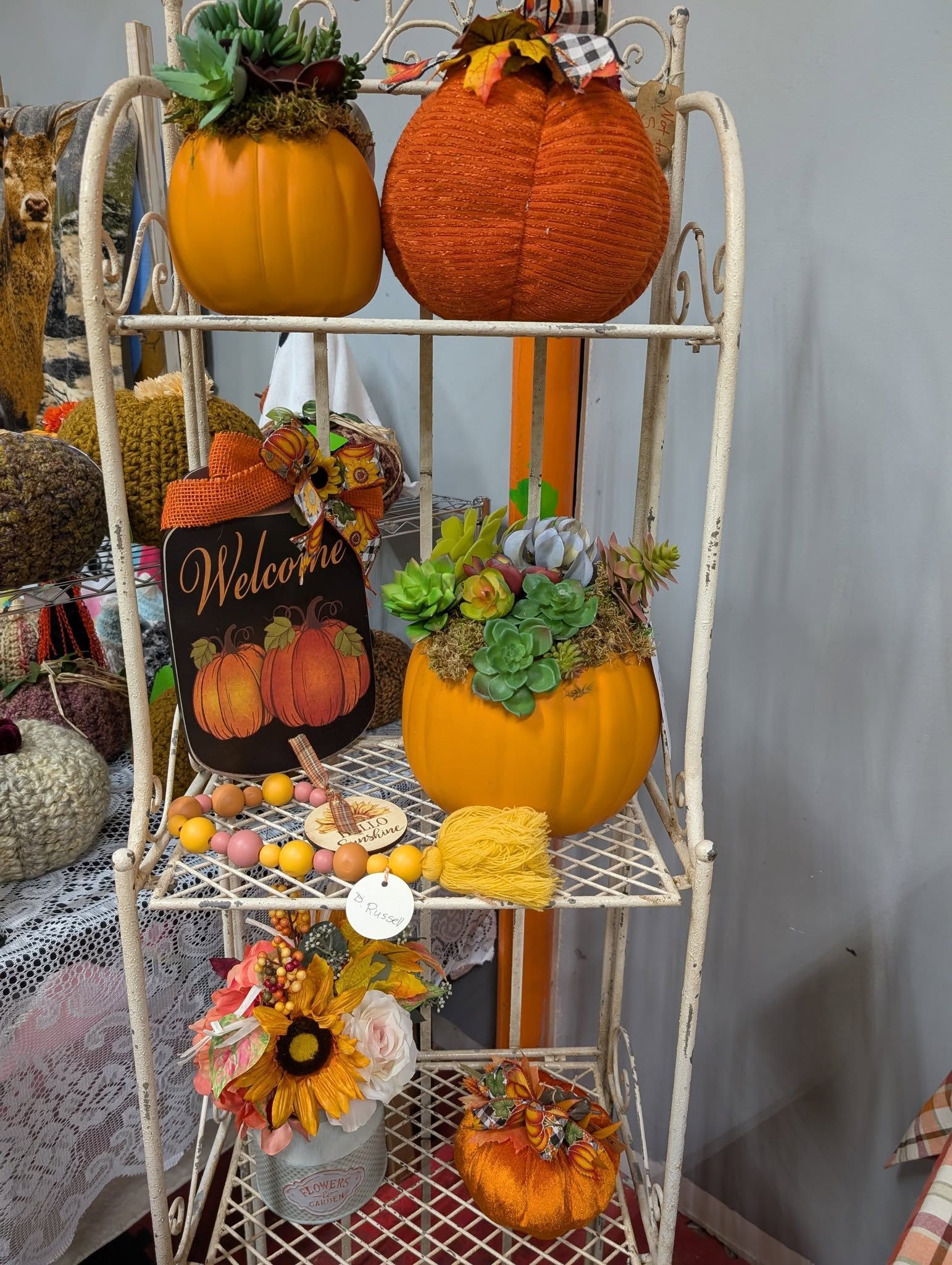 White metal shelf decorated with fall-themed pumpkins, succulents, and seasonal decorations.