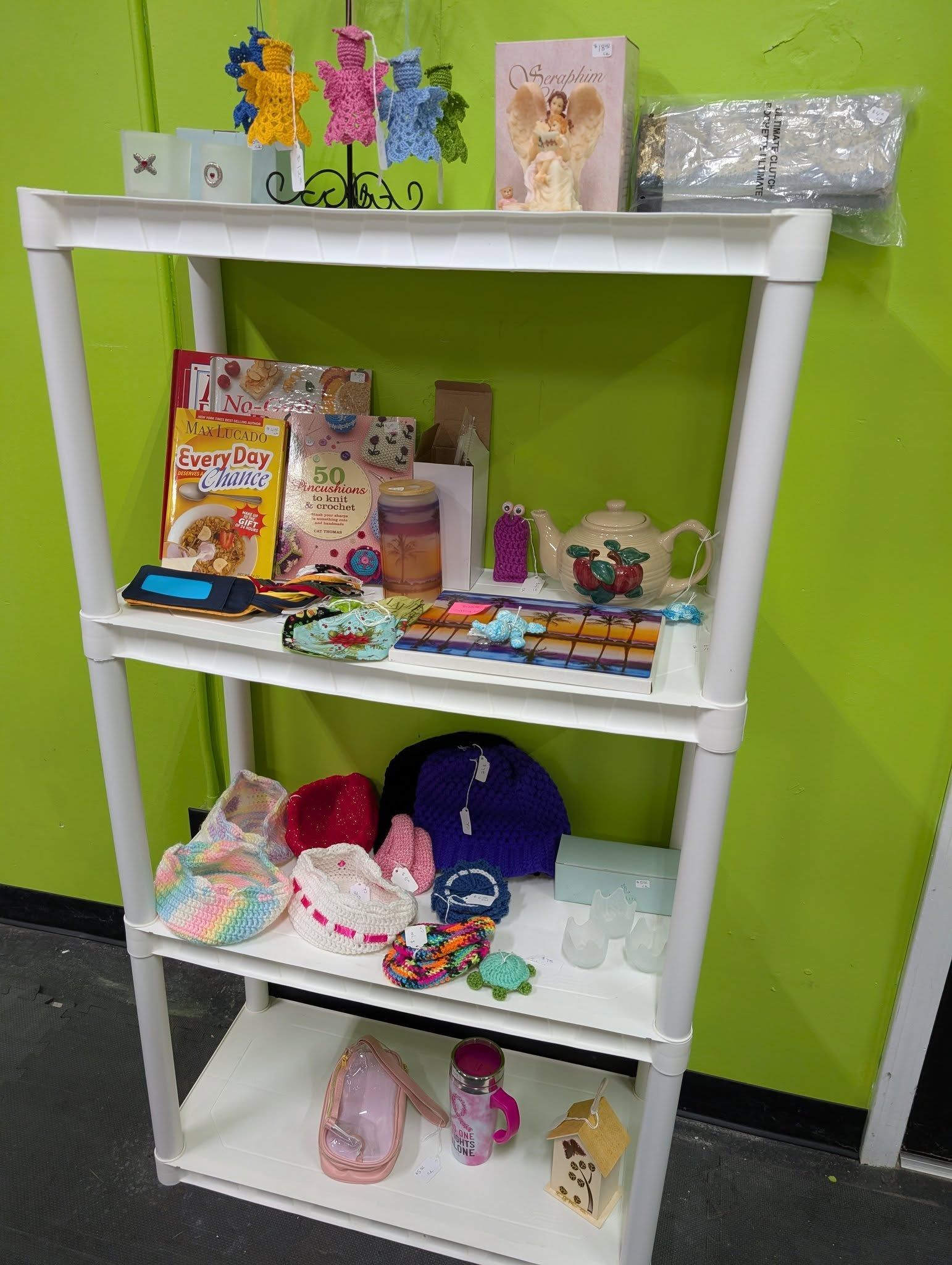 White shelving unit with various craft and decorative items on each shelf, against a green wall.
