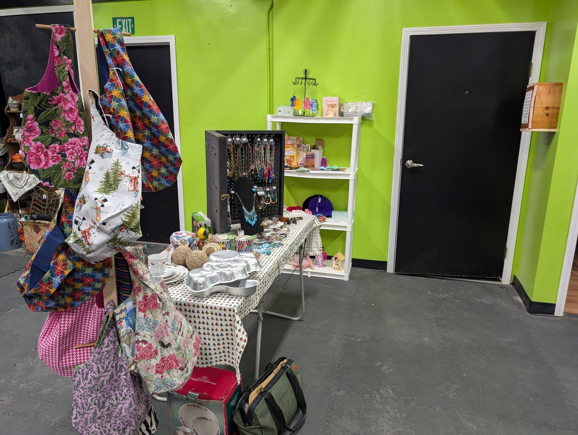 A shop interior with a table displaying jewelry and bags hanging from a rack, against bright green walls.