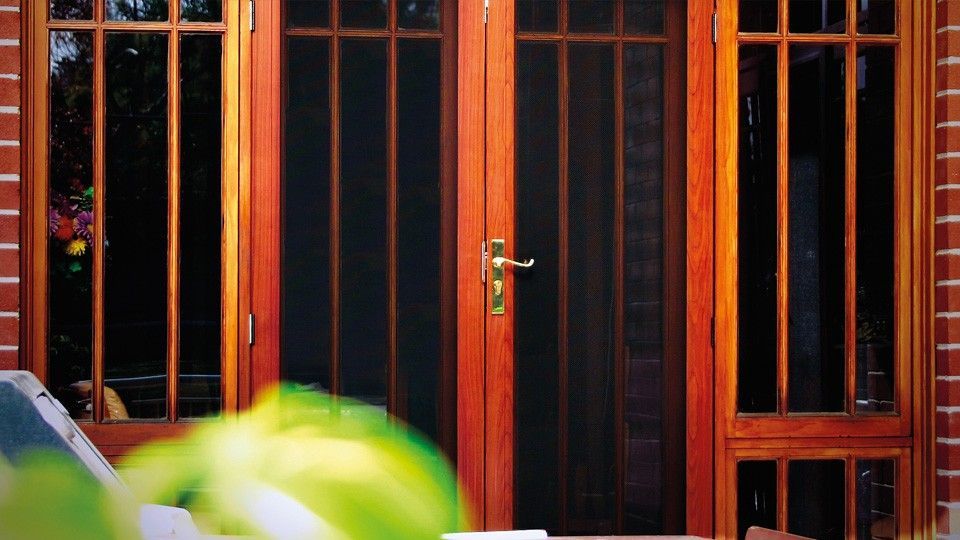A Wooden Door With a Screen on It is Sitting in Front of a Brick Building — Whitsunday Screens & Grilles In Proserpine, QLD