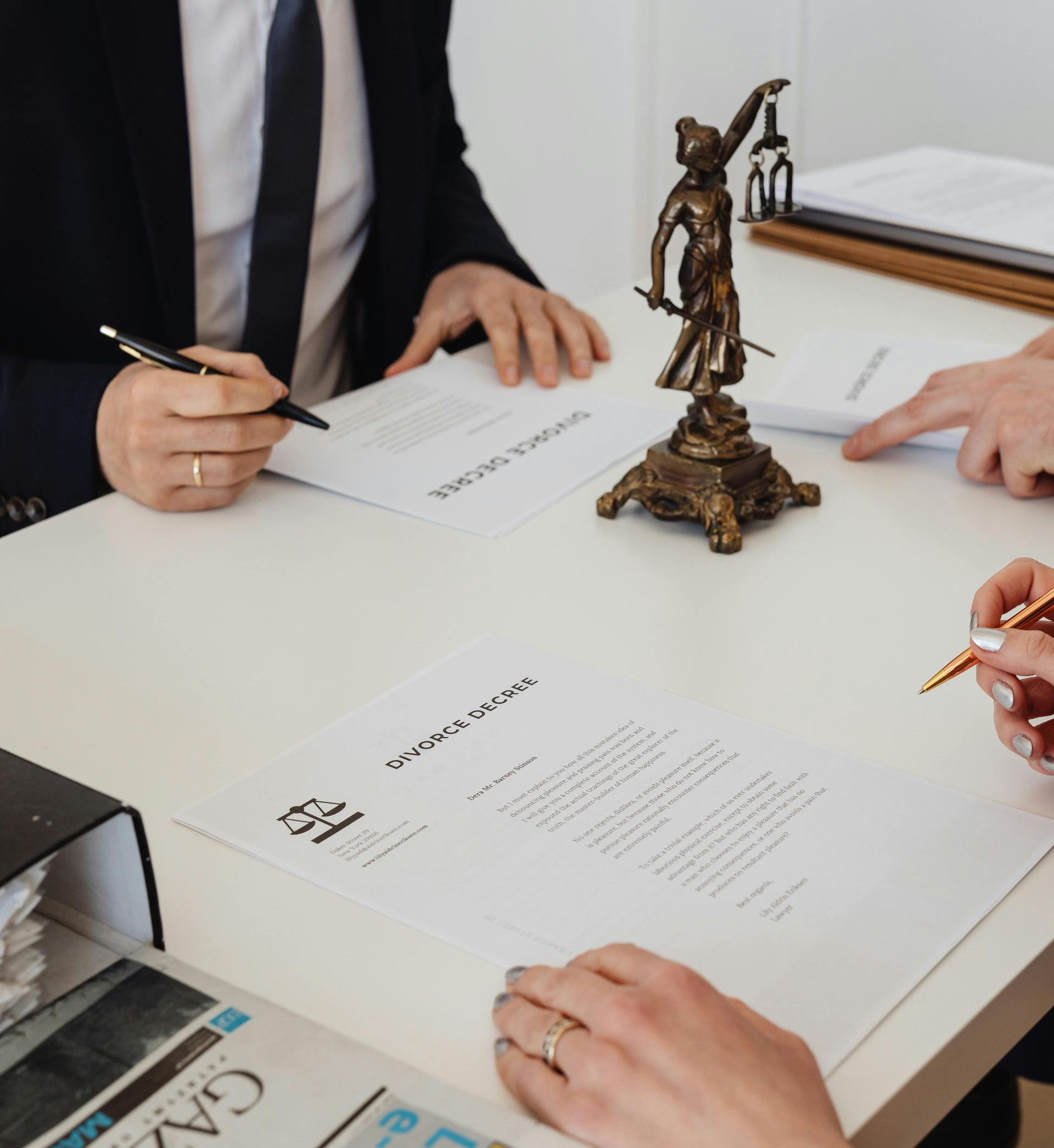 Pessoas assinando documentos legais em uma mesa ao lado de uma pequena estátua da justiça.