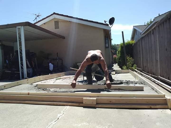 A man is flating concrete on a sidewalk with a wood