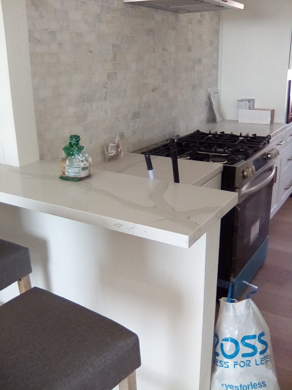 Kitchen with quartz countertop, gas range, white cabinets, and decorative backsplash.