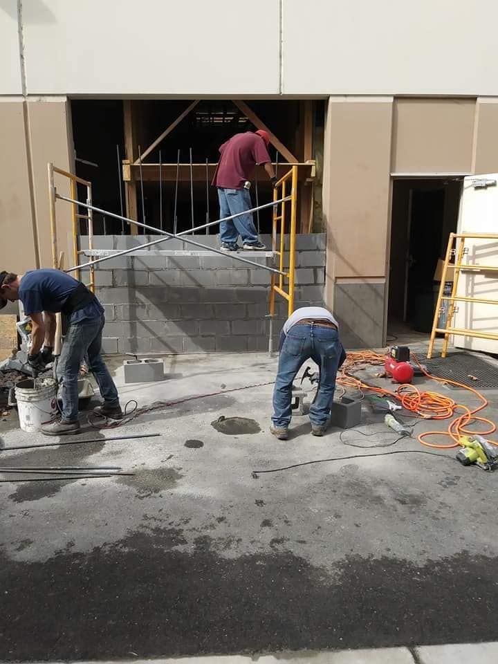 Three construction workers building a doorway, with brick blocks, a yellow scaffolding, and tools.