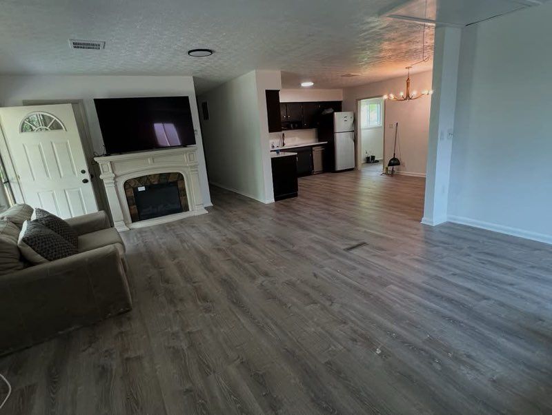 Spacious living room with fireplace, TV, open to kitchen with dark cabinets, and a chandelier.