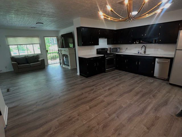 Spacious open-concept living space with a kitchen. Black cabinets, wooden floor, large windows, and a sofa.