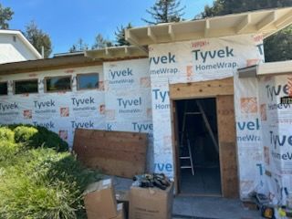 Exterior of a building under construction, wrapped in Tyvek, with an open doorway and boxes outside.