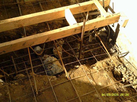 Construction site with wooden frame and wire mesh laid on ground. Concrete work in progress.
