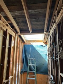 Interior view of a room under construction. Wooden frame with ladder, tarp, and exposed ceiling beams.