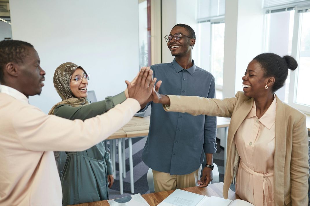A group of people are giving each other a high five in an office.