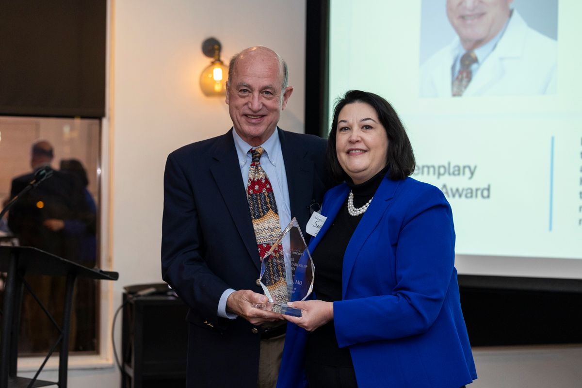 A woman with red hair is wearing a blue shirt and a black jacket