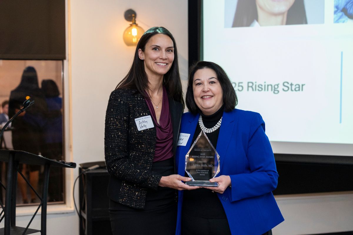 A man in a white coat and tie is wearing glasses.