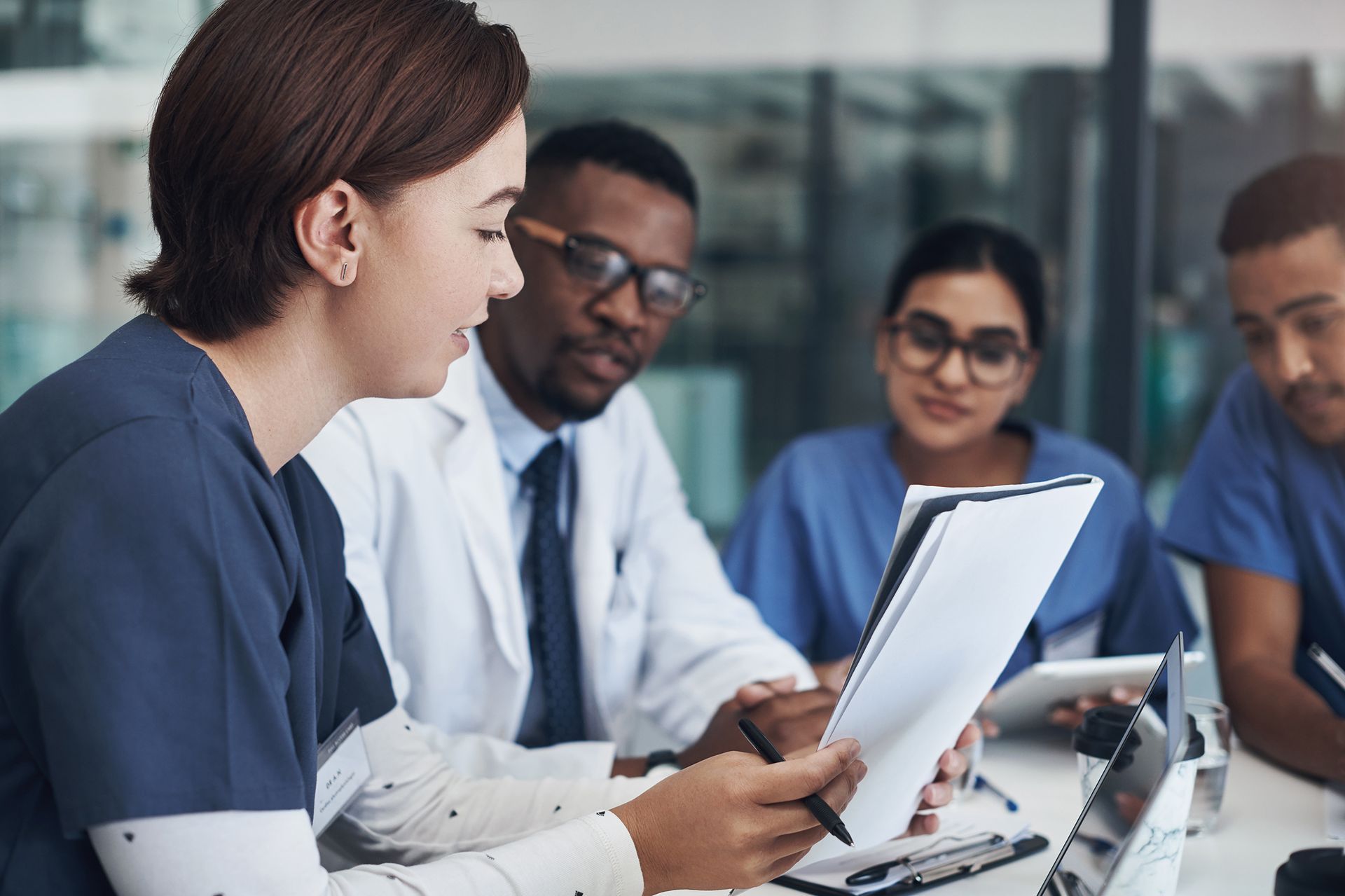 A group of doctors and nurses are having a meeting and looking at a clipboard.