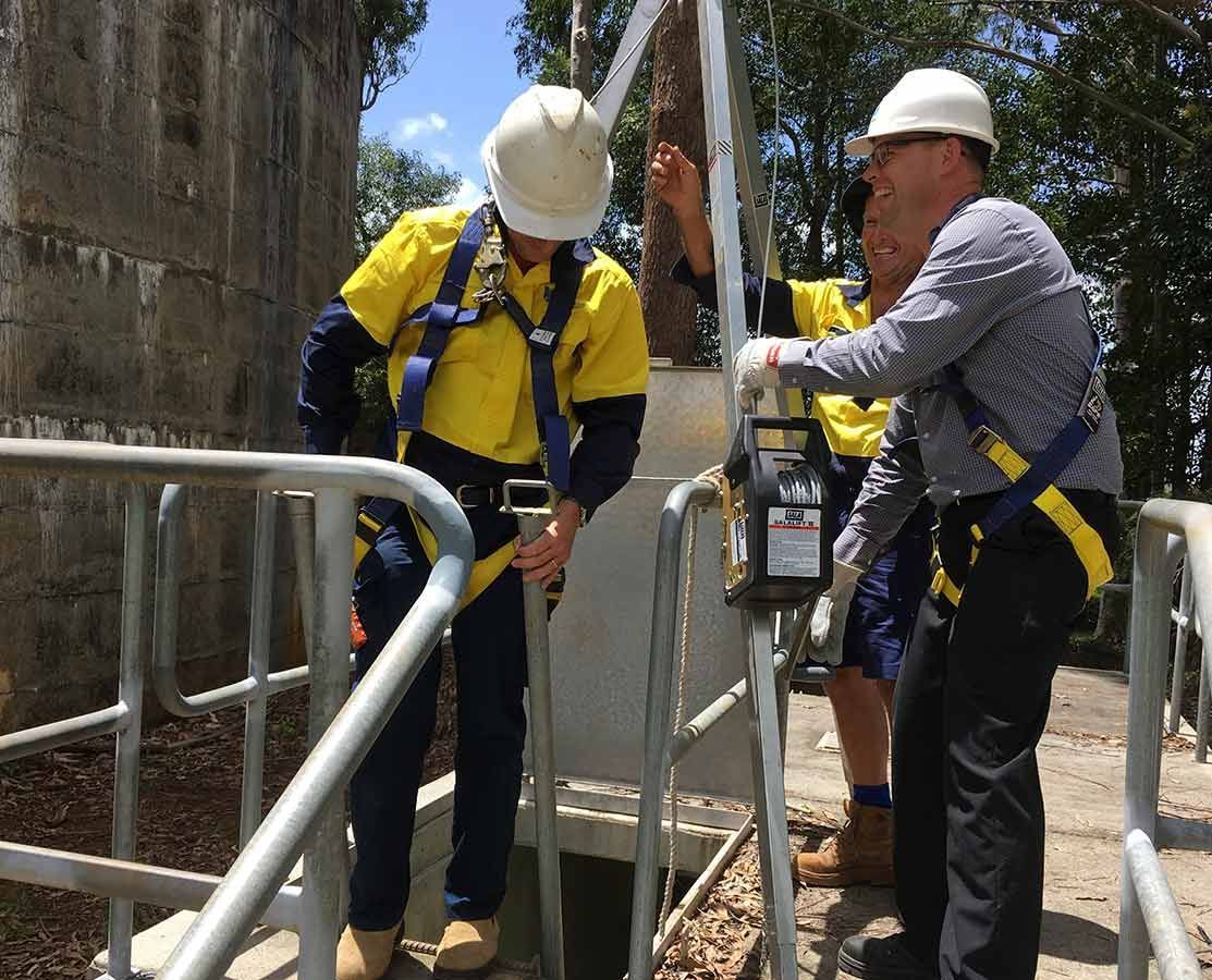 A Group Of Men Wearing Hard Hats And Safety Harnesses Are Working On A Fence — NCA Consulting Pty Ltd in Alstonville, NSW