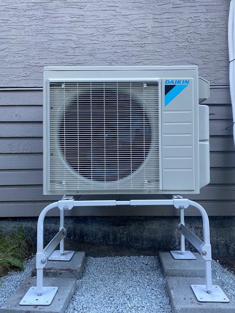White air conditioning unit on a white metal frame, mounted on concrete blocks, next to a beige building.