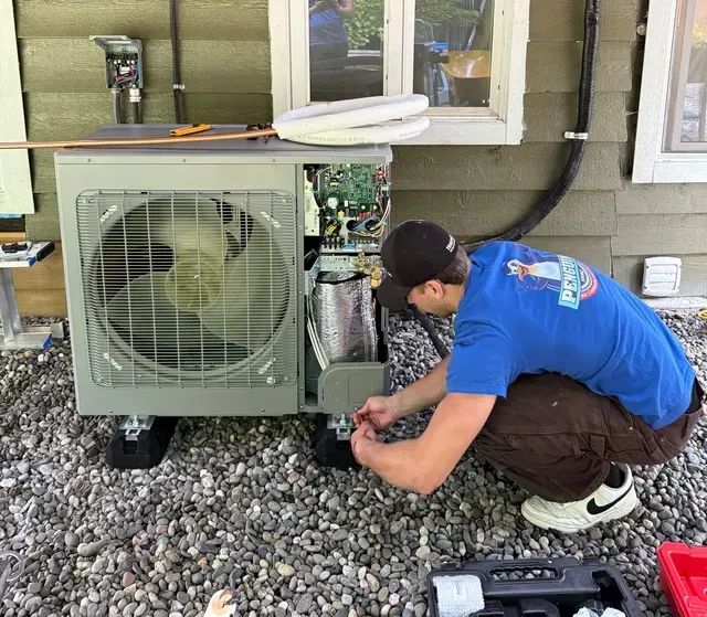 Man working on the open interior of an outdoor HVAC unit, near a building.