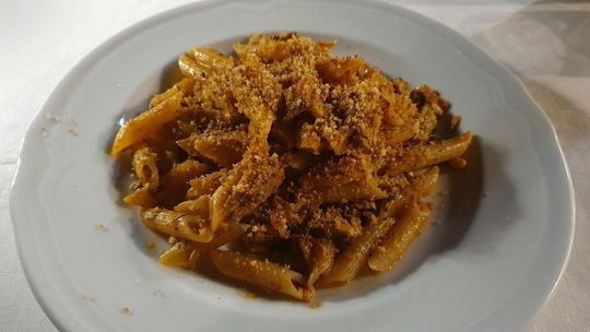 Piatto di pasta al sugo di pomodoro e formaggio grattugiato su un piatto bianco.