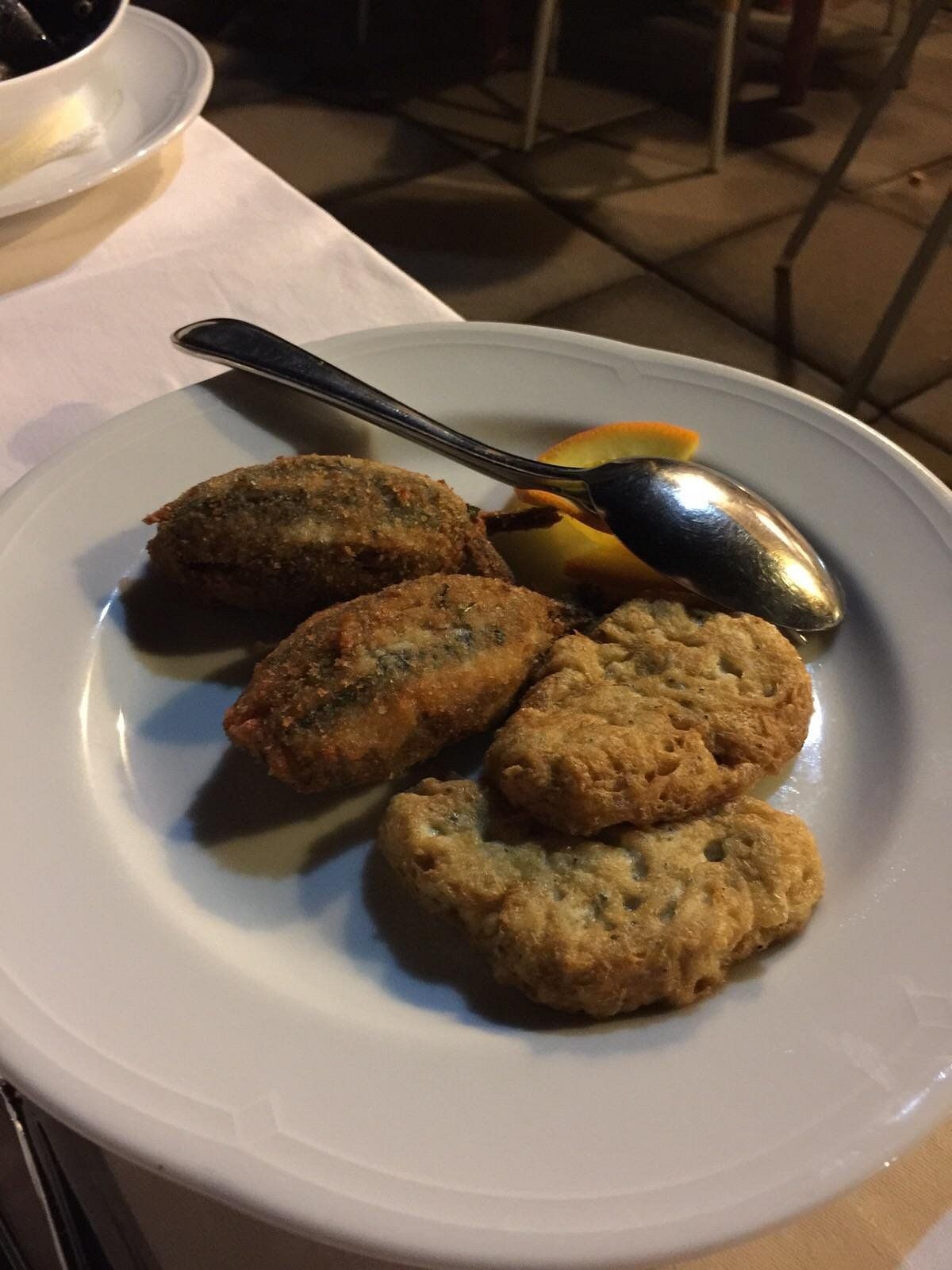 Un piatto di crocchette fritte su un piatto bianco con cucchiaio e tovagliolo su un tavolo di ristorante.