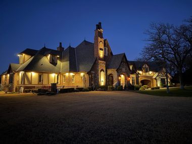 Large stone house lit warmly at dusk, with a dark blue sky and trees around it