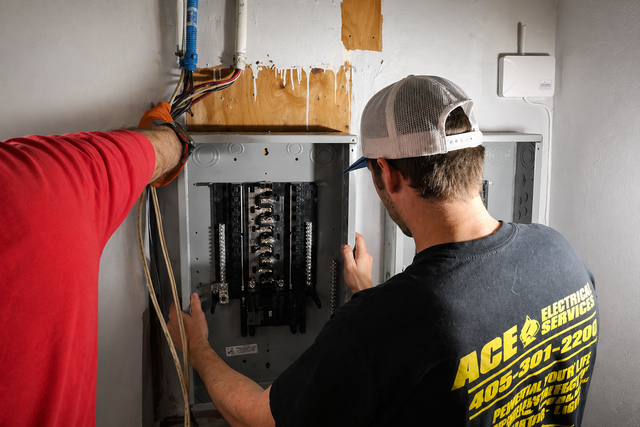 Electrician on a ladder fixing a kitchen ceiling light beside an open electrical breaker panel