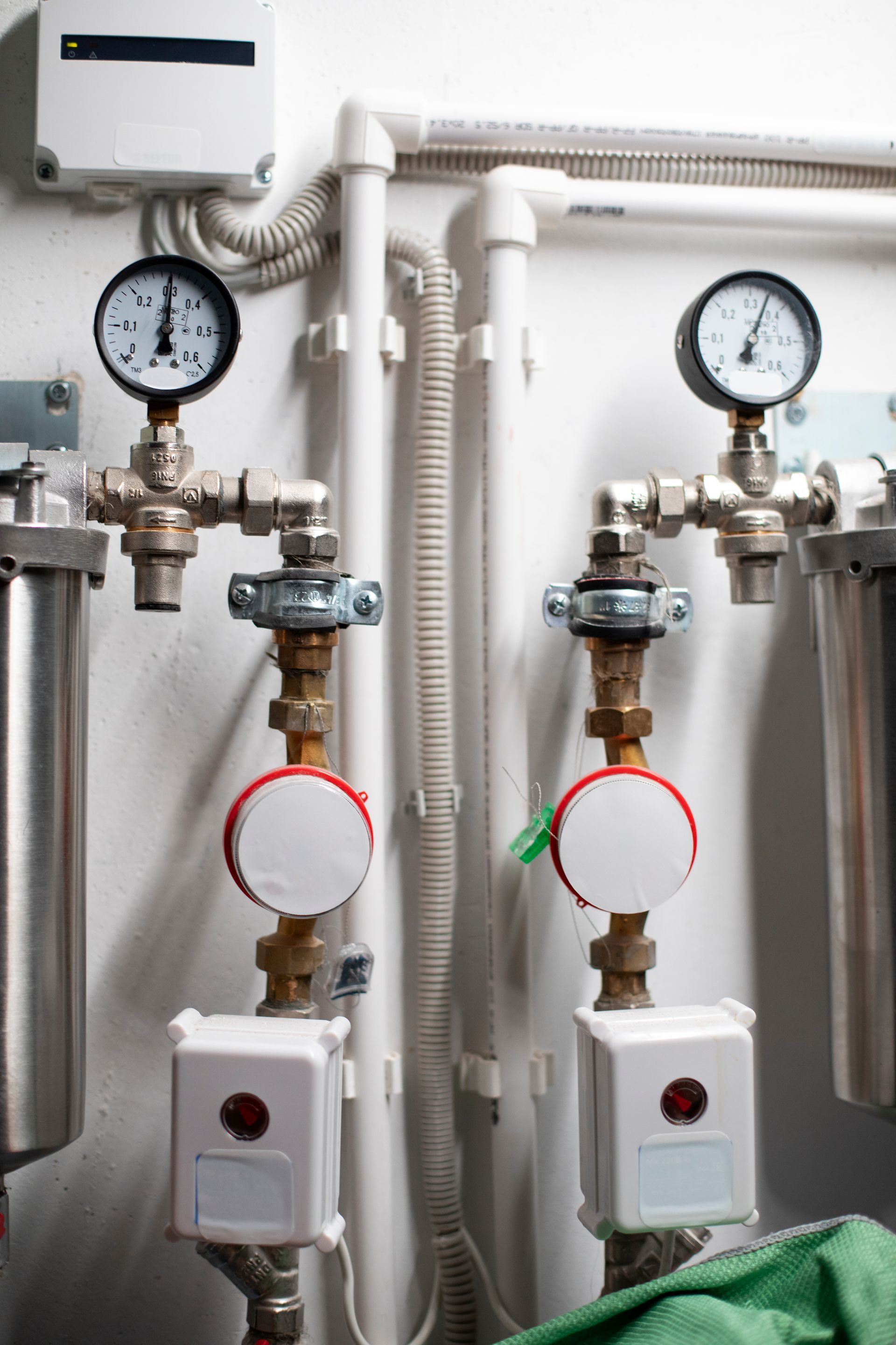 Two parallel water filtration systems on a white wall, each featuring a pressure gauge, a water meter, and an electronic box.