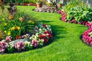 Colorful flower beds lining a lush green garden path with potted plants in the background
