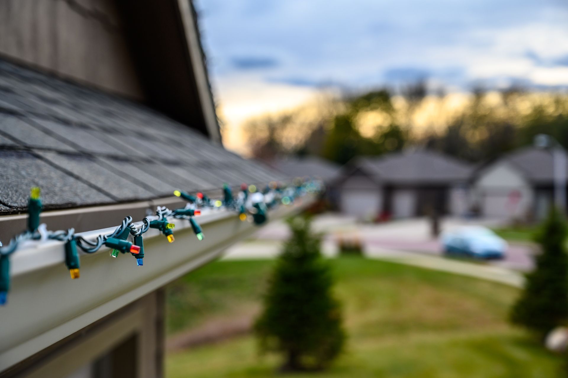 String lights clipped along a roof edge, overlooking a blurred suburban yard at dusk