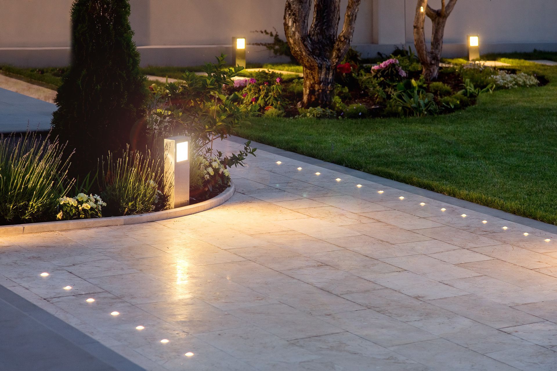 Lit stone walkway beside a grassy garden, with small pathway lights at dusk