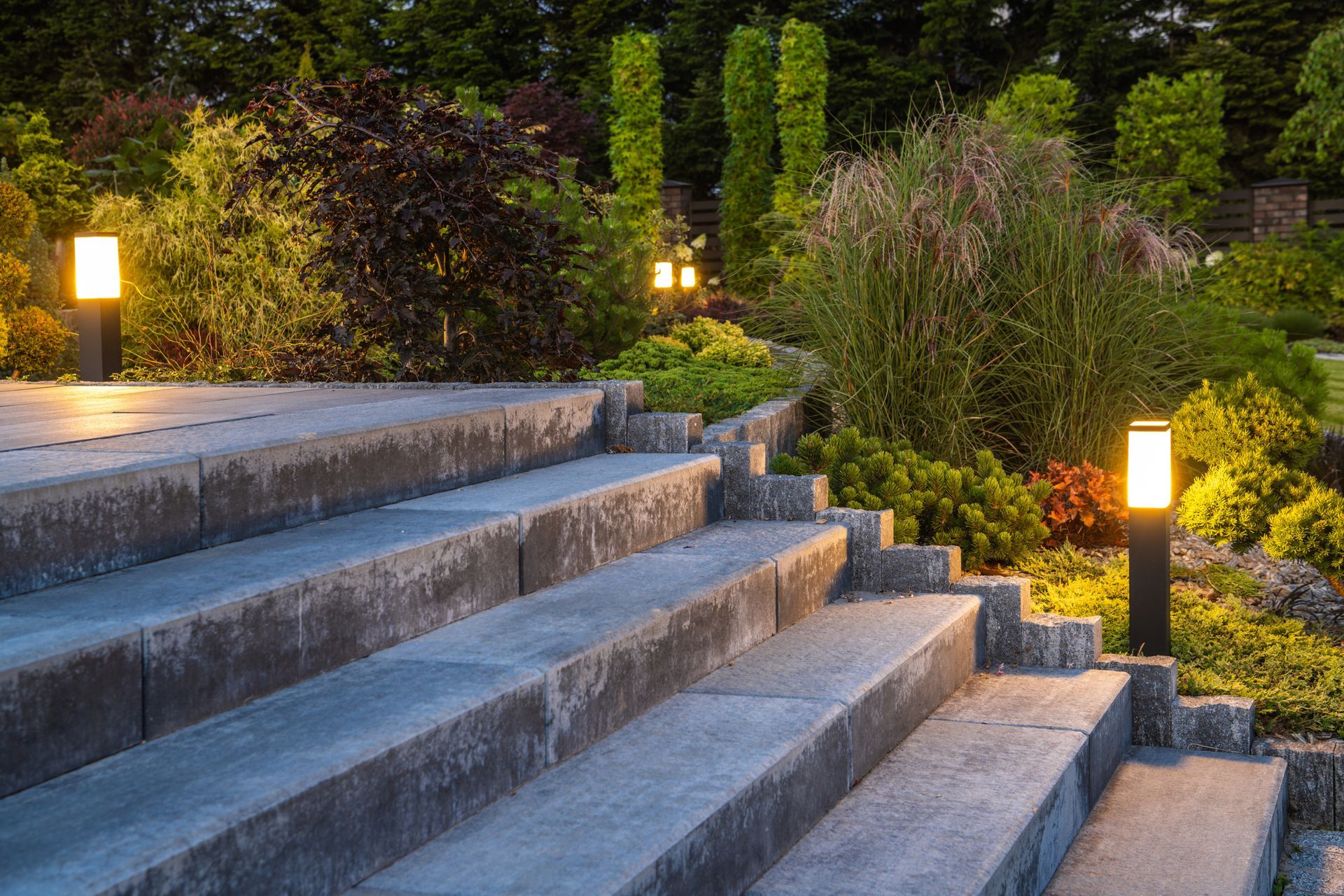 Stone steps in a landscaped garden lit by small glowing path lights at dusk