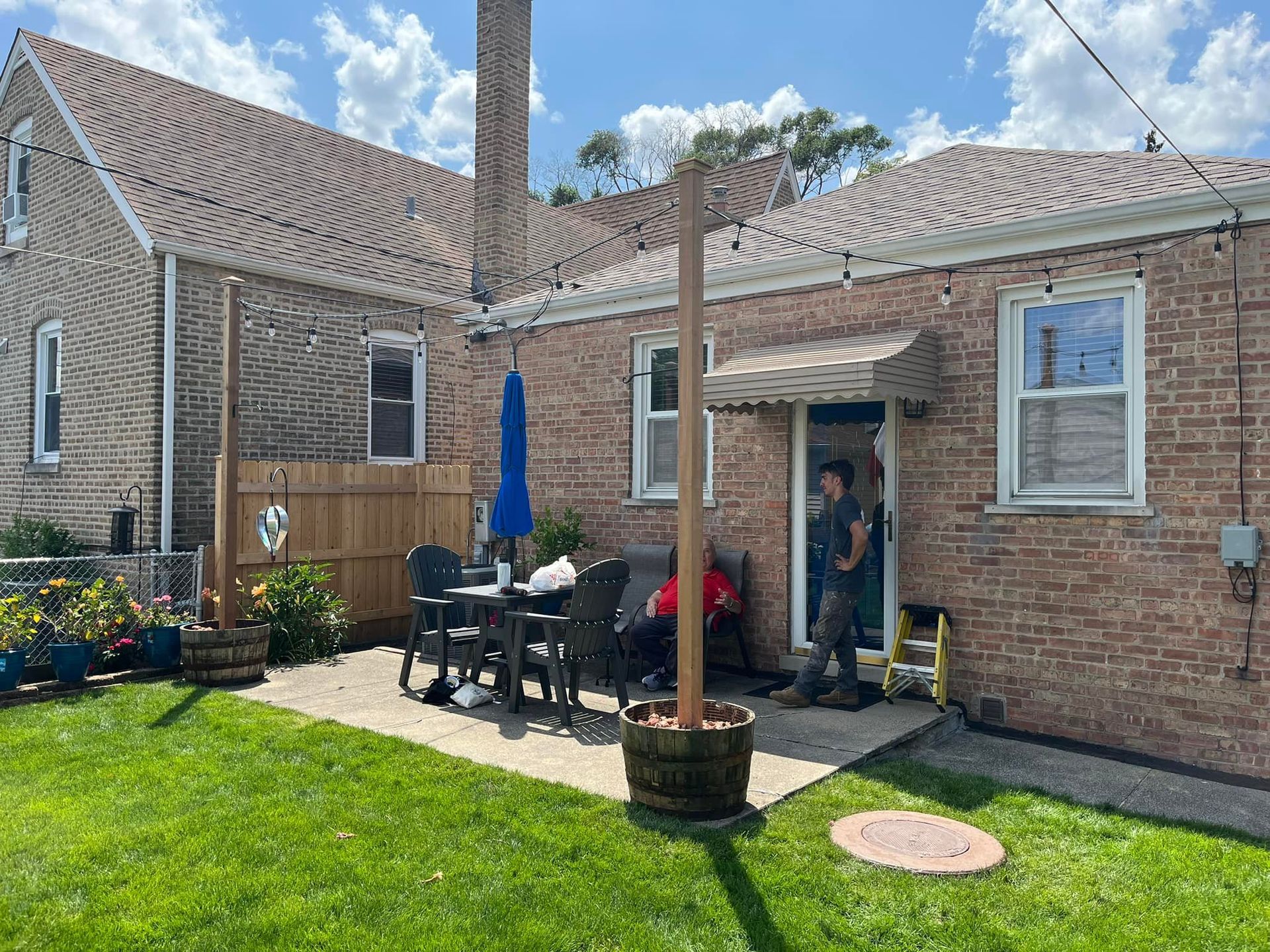 A man is standing in front of a brick house with a patio in front of it.