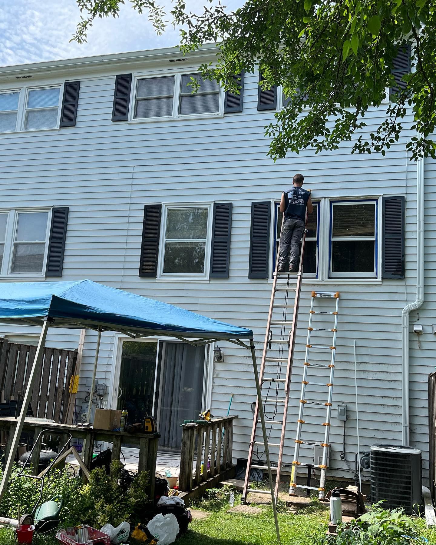 A man is standing on a ladder on the side of a white house.