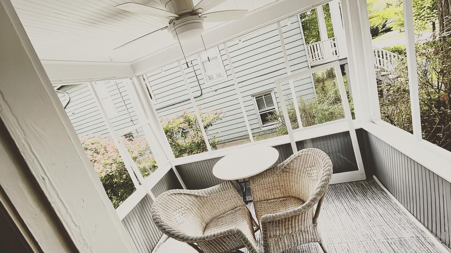 A screened in porch with wicker furniture and a ceiling fan.