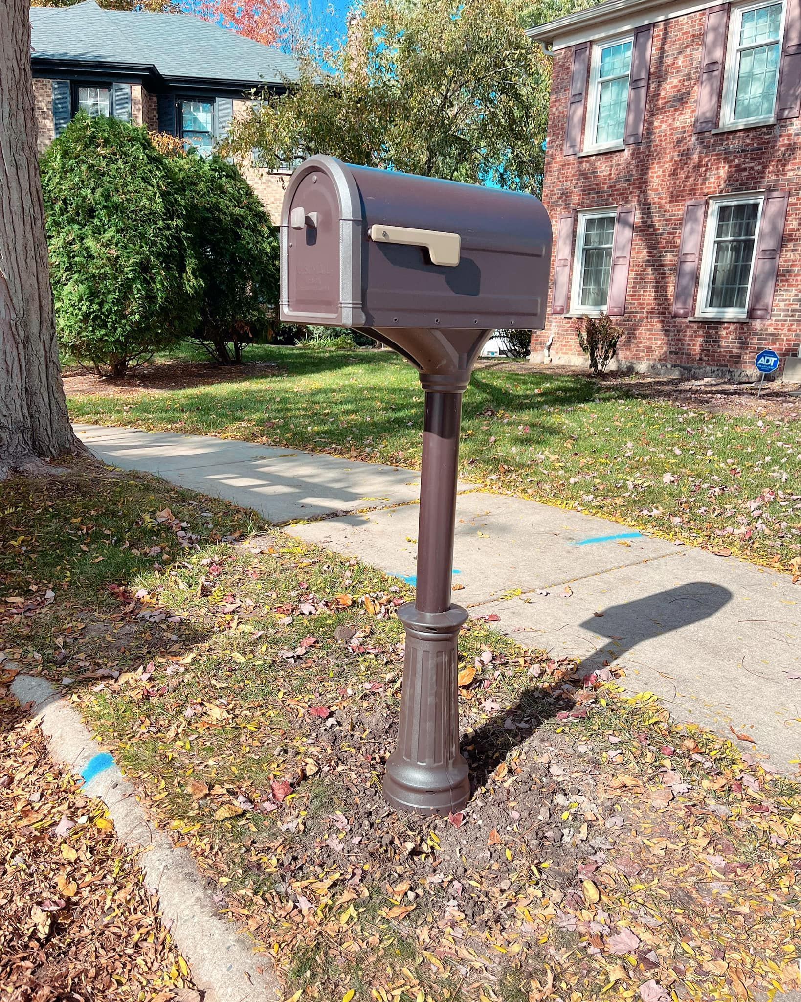 A mailbox is sitting on the sidewalk in front of a brick house.