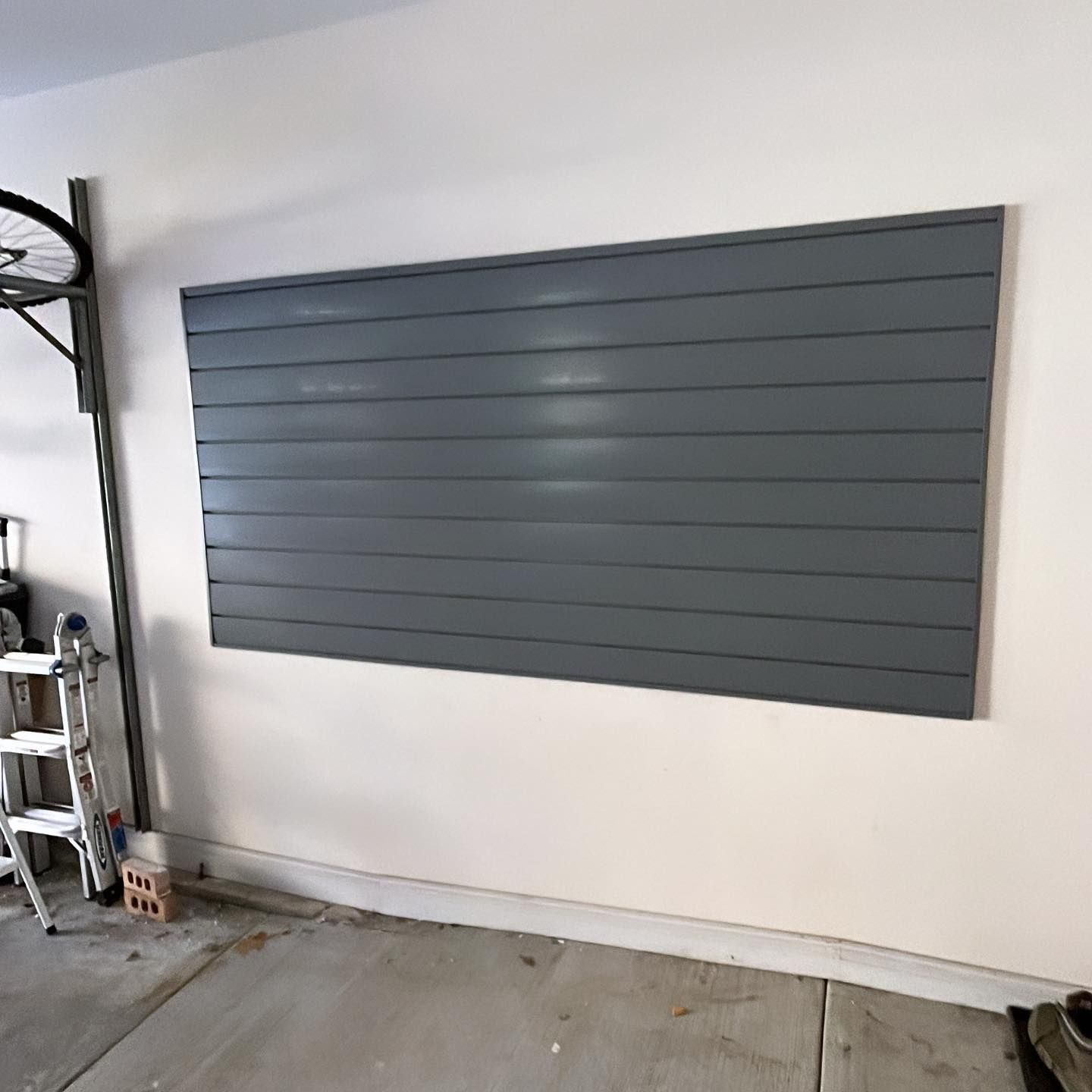 A large gray wall is hanging on a white wall in a garage.