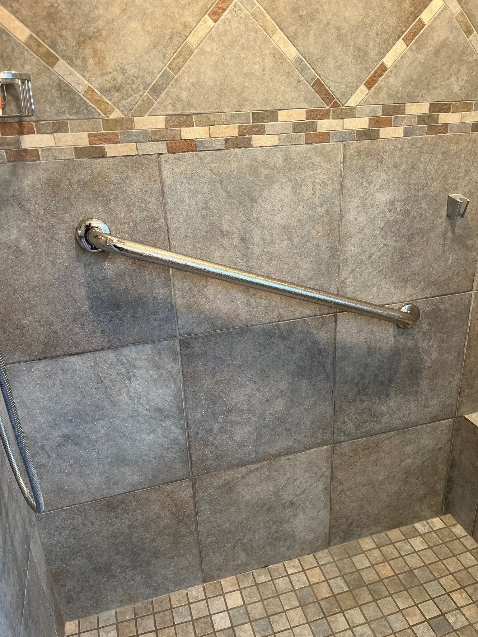 A shower with a handle on the wall and a tiled floor.