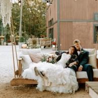 Couple relaxing on a white outdoor sofa at a rustic patio swing, wrapped in a fluffy white blanket