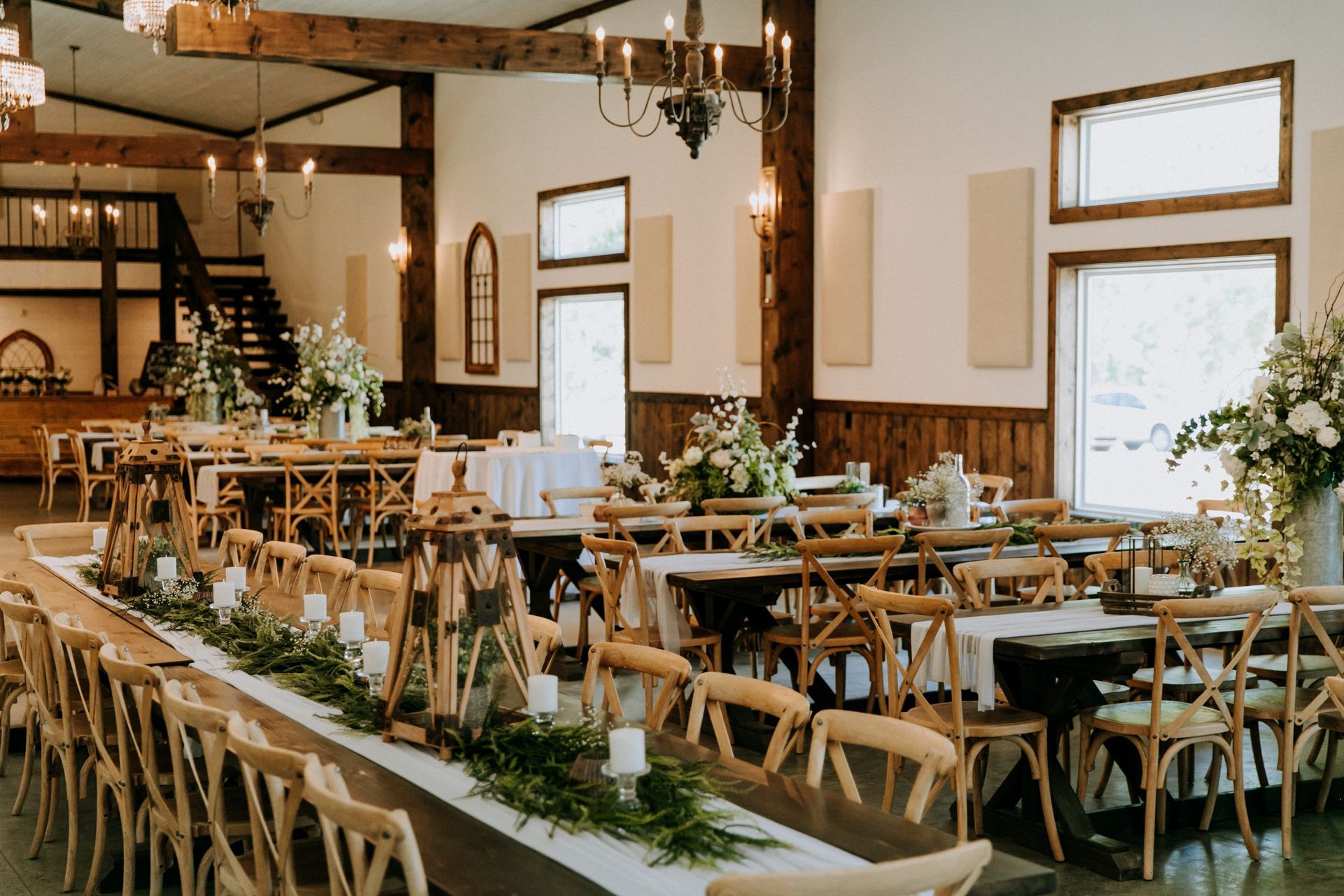 Rustic banquet hall with long tables, wooden chairs, white tablecloths, and floral arrangements