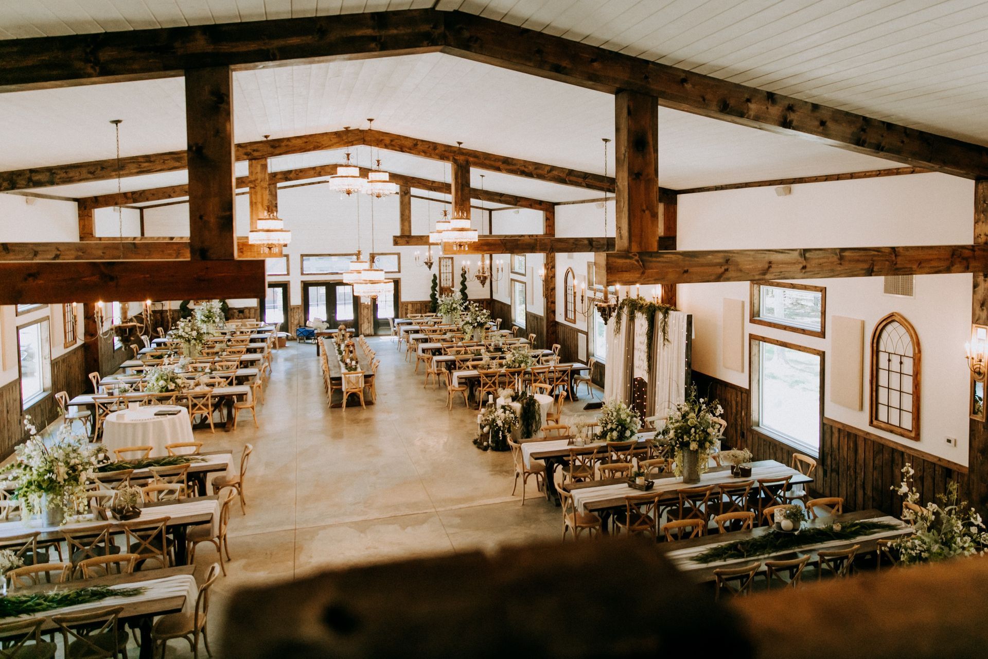 Rustic banquet hall with long tables, wooden beams, and natural light from large windows