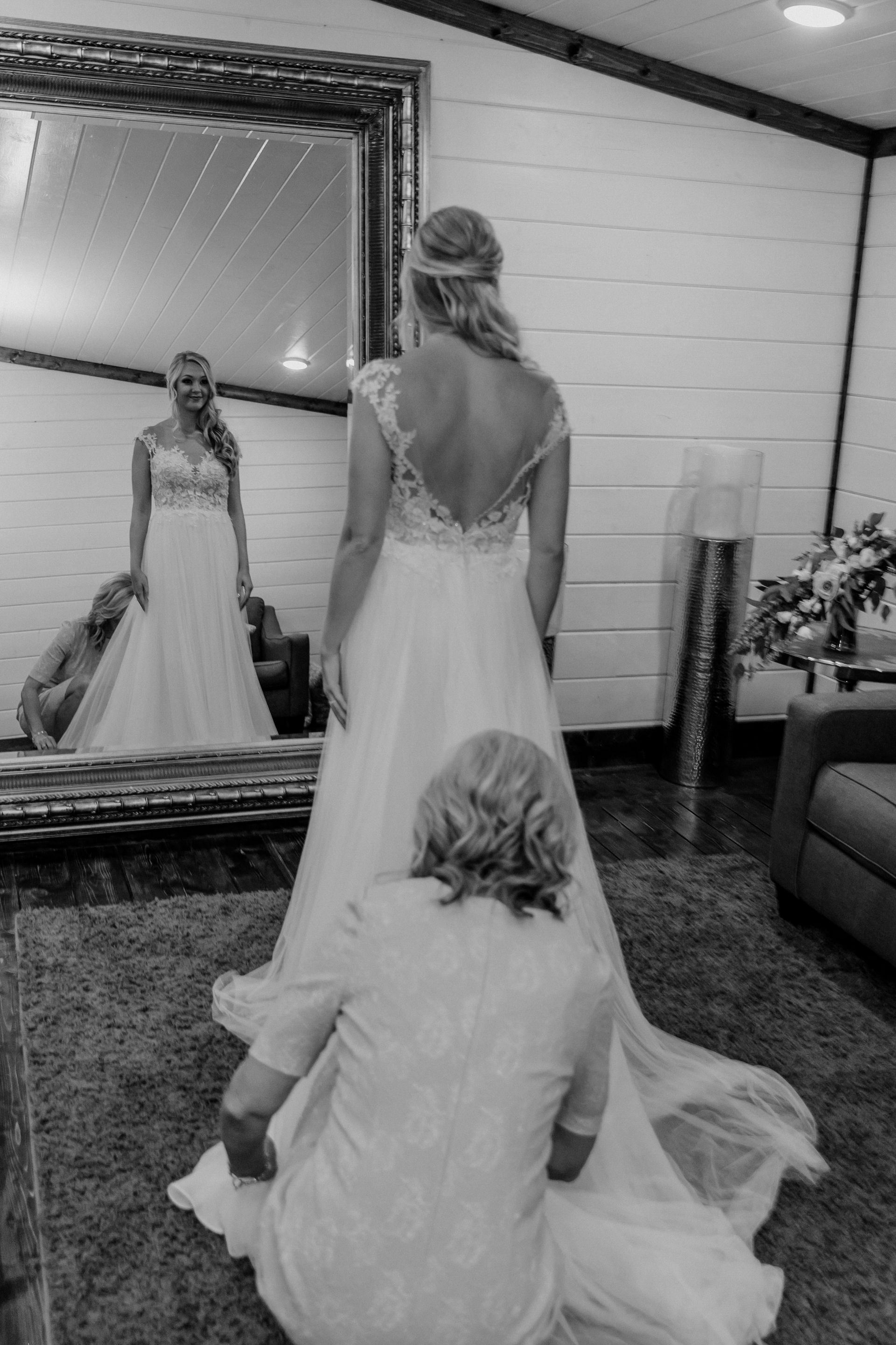 Bride in a white gown kneels before a mirror, looking at her reflection in a bridal suite