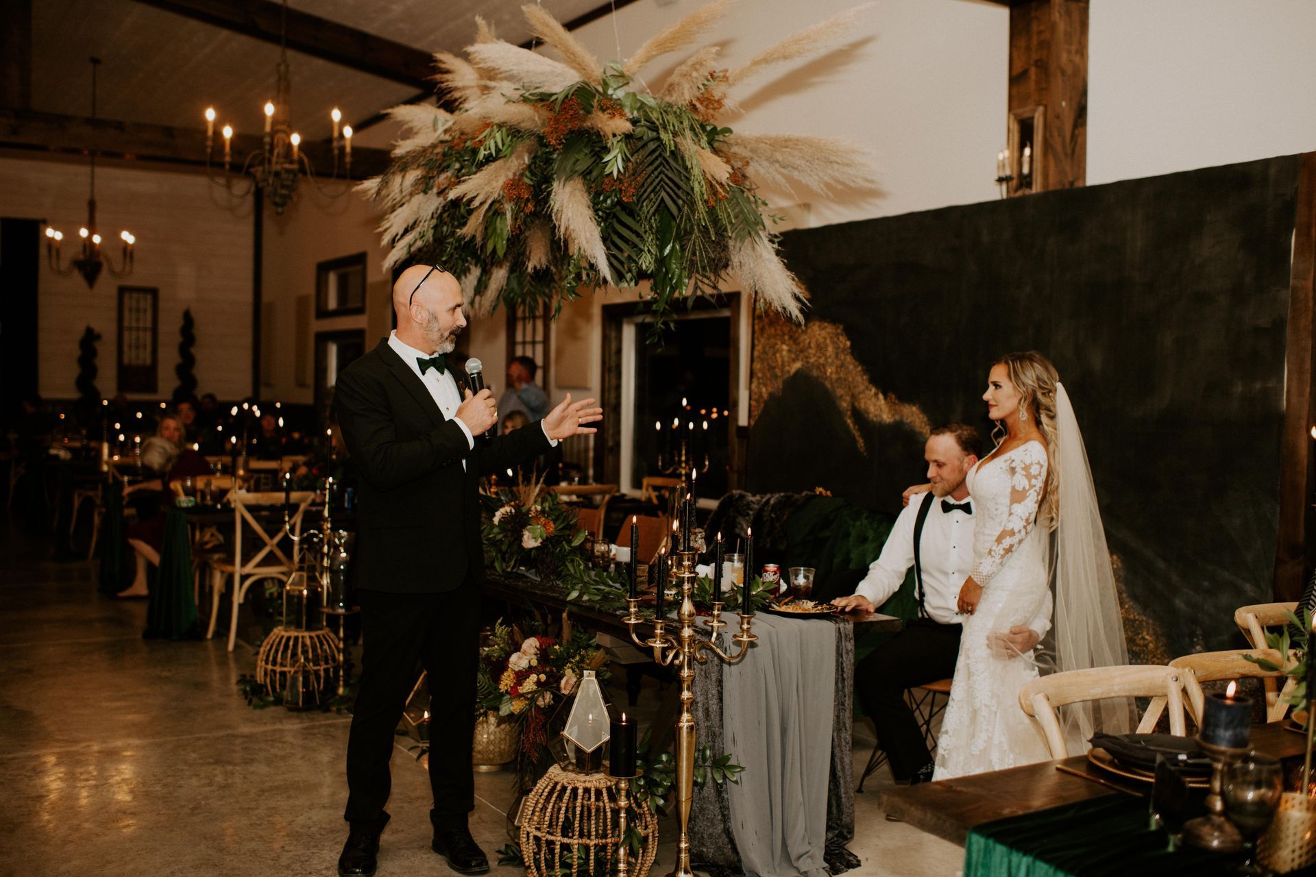 Wedding ceremony indoors as officiant speaks beside the bride and groom under floral decor