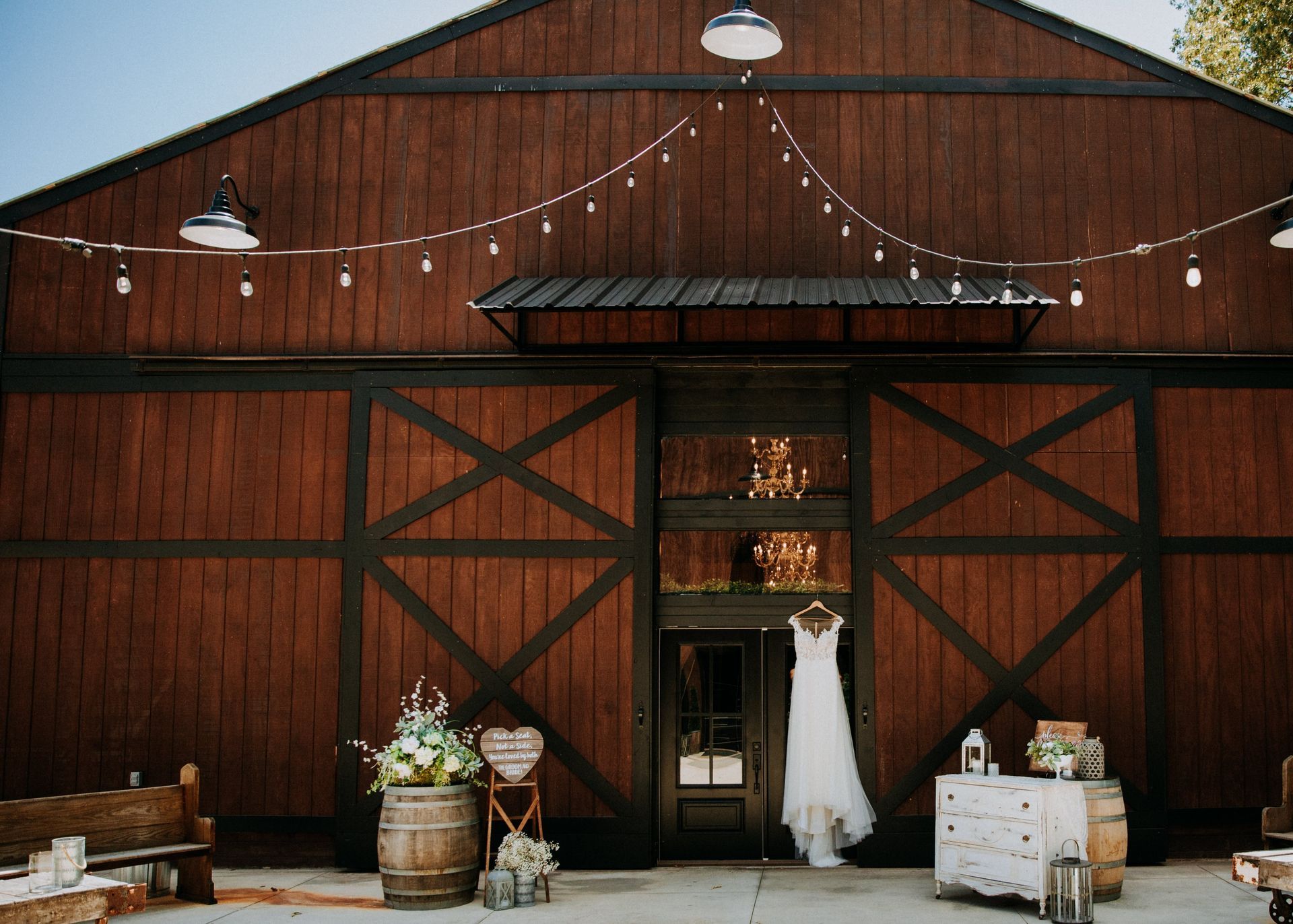 Rustic barn wedding entrance with string lights, floral decor, and a wedding dress in the doorway