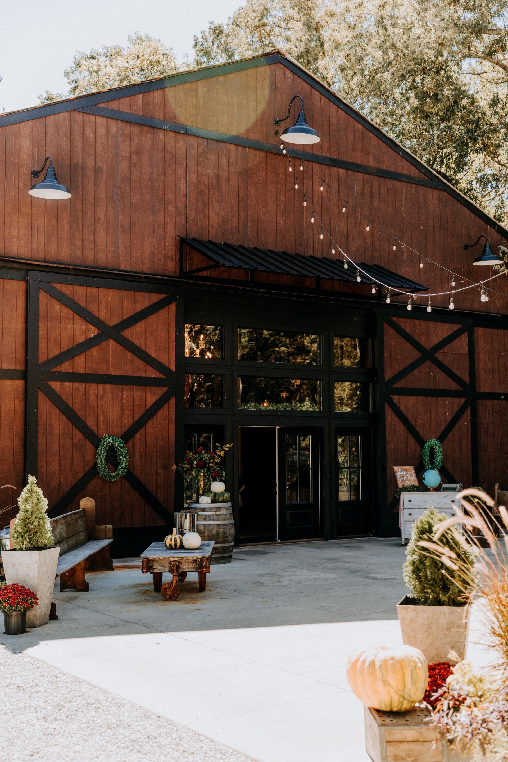Rustic red barn entrance with black trim, hanging lights, and fall decor at a storefront entrance